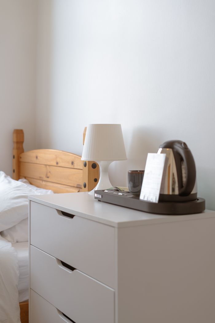 Minimalist bedroom with white drawers and wooden bed in a Derby hotel room.