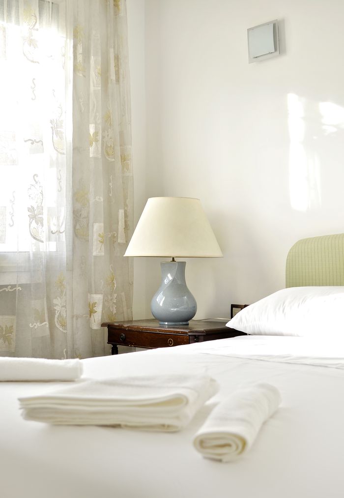 Bright and cozy hotel room interior featuring a neatly made bed, soft linens, and a stylish lamp on a wooden nightstand.